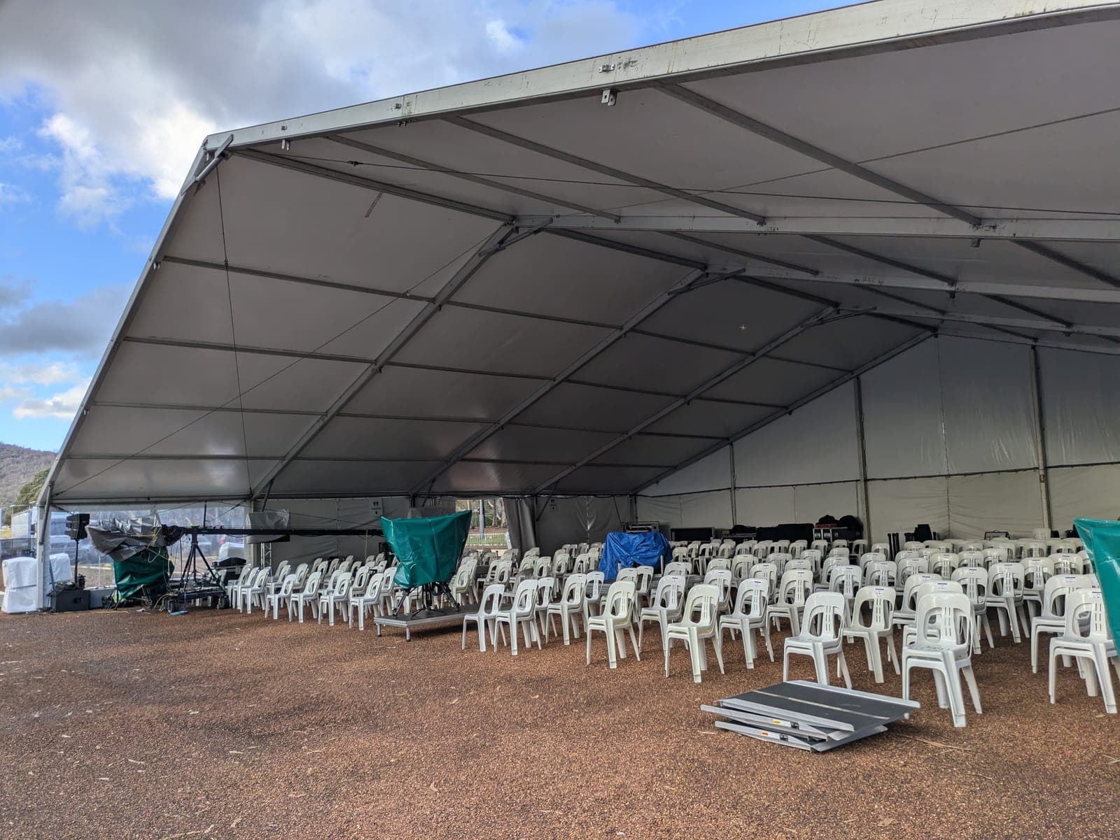 A large clear-span marquee with an aluminium portal frame, set out with rows of white plastic chairs on gravel ground