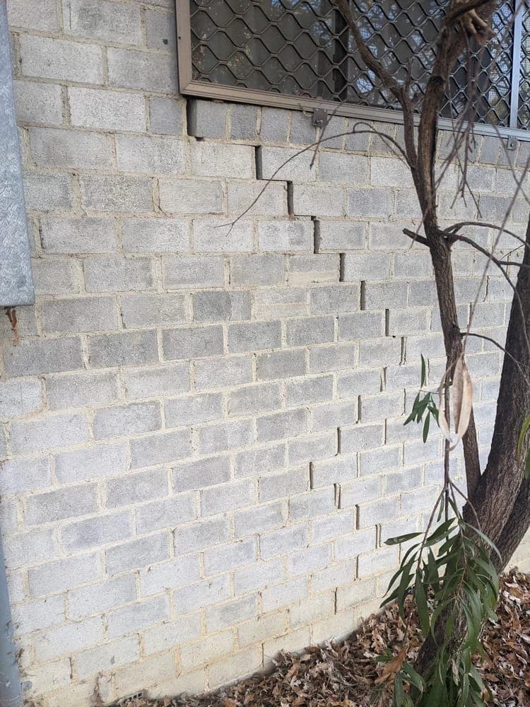 A stepped crack running down through the mortar joints of a concrete block wall, from beneath a window towards the ground