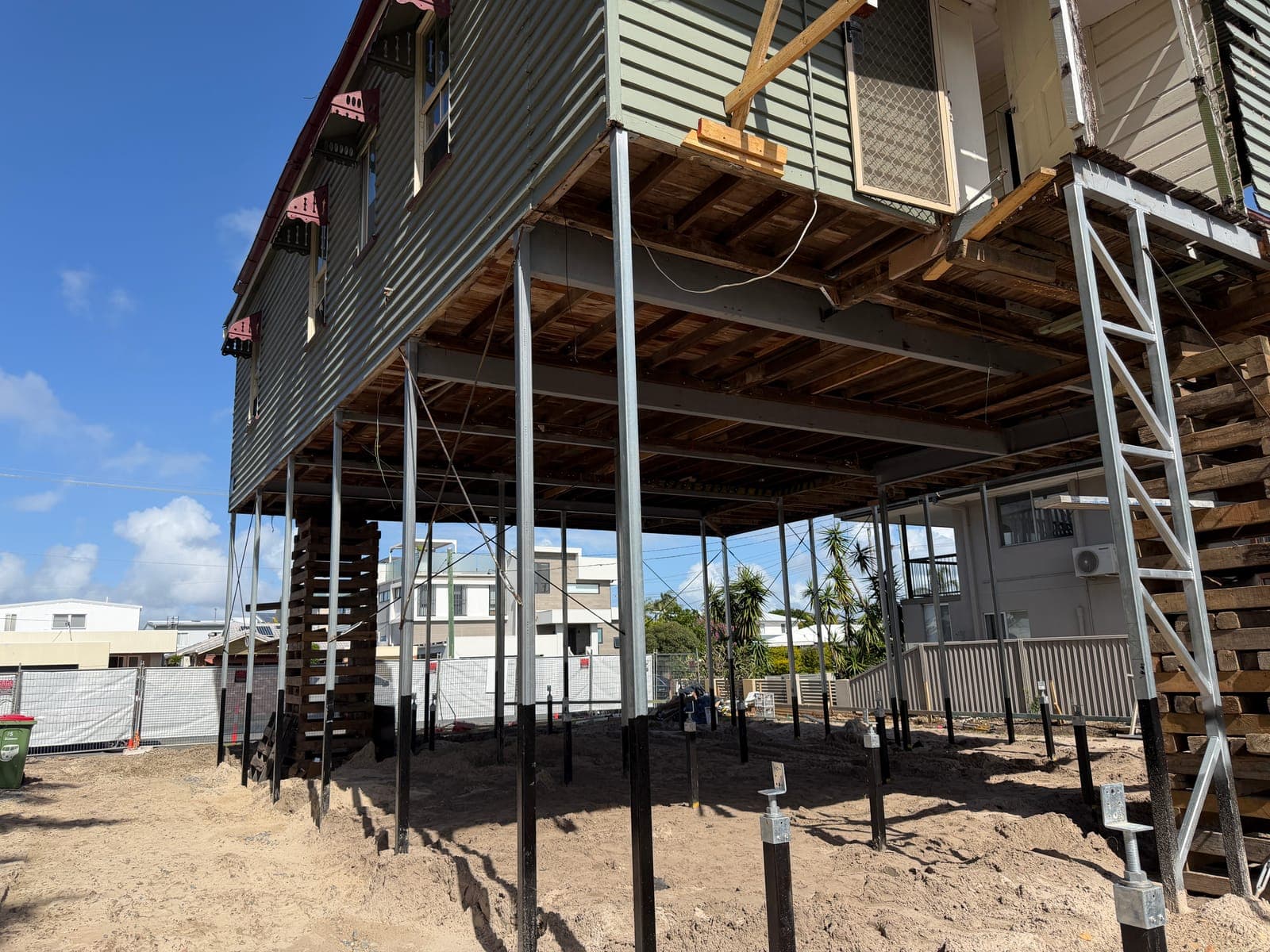 The house suspended on steel props above the sand, with black pile heads projecting from the ground beneath it