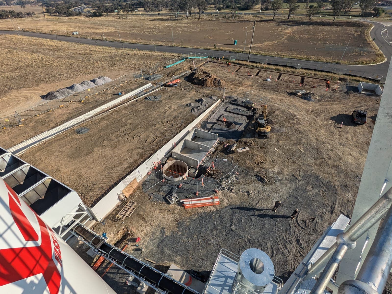 Elevated view down onto the plant site, showing a long retaining wall, excavated foundations, a circular pit and an excavator at work